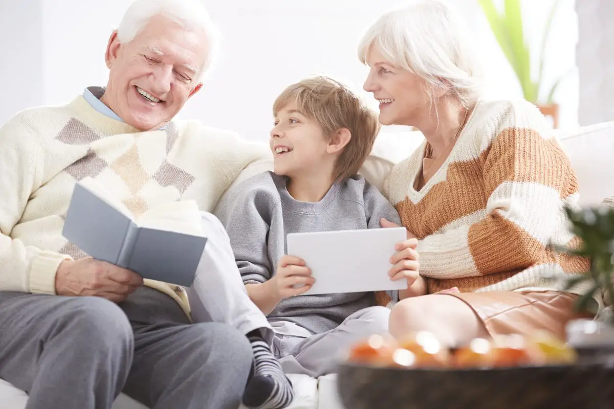 Grandfather reading the book next to grandson with tablet