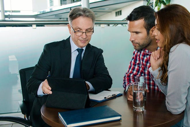 A couple meets with a financial advisor, looking concerned at a tablet screen.