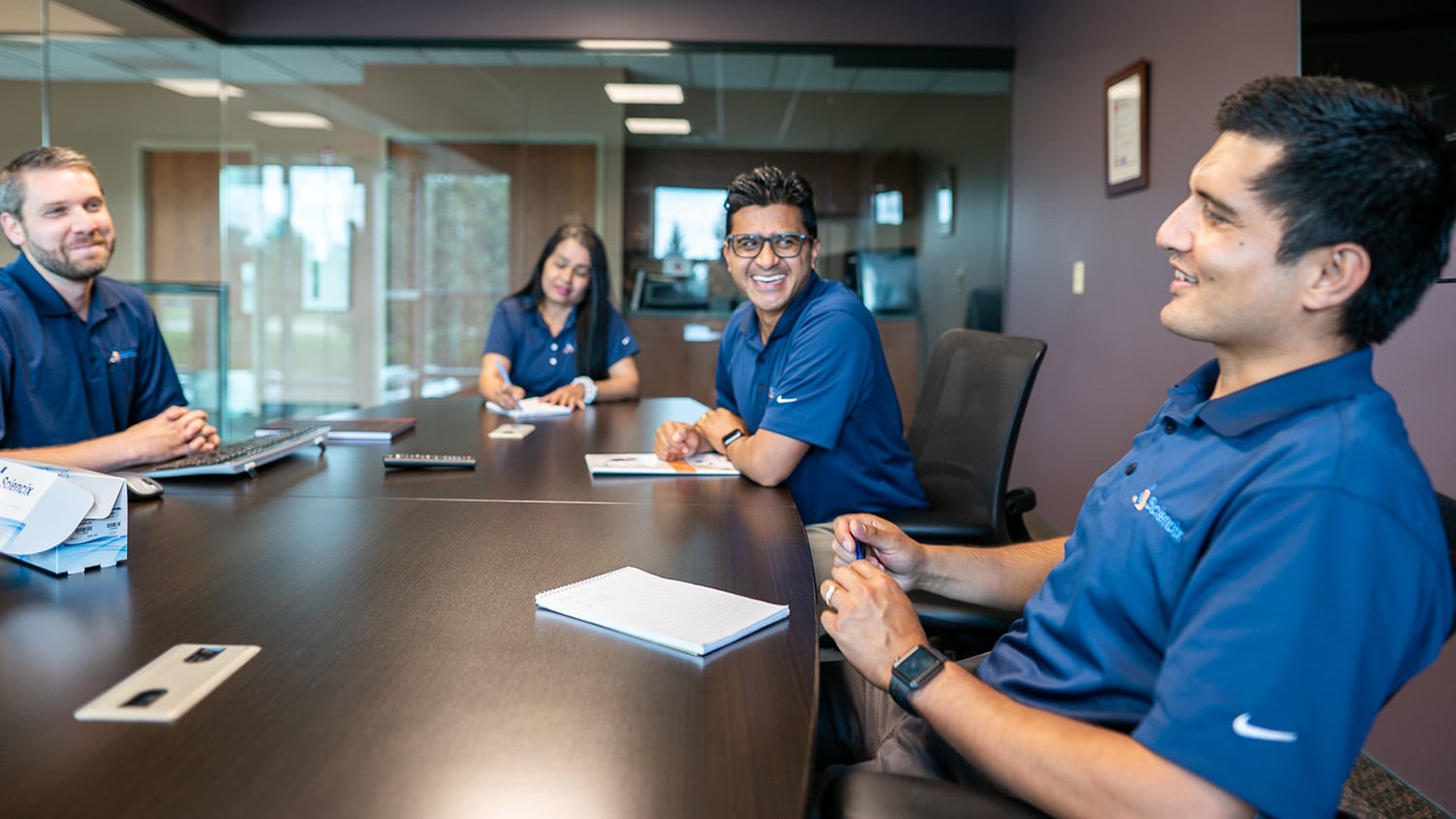 Members of Sciencix sit around a conference table and talk. They are wearing matching blue polos with the company's logo.
