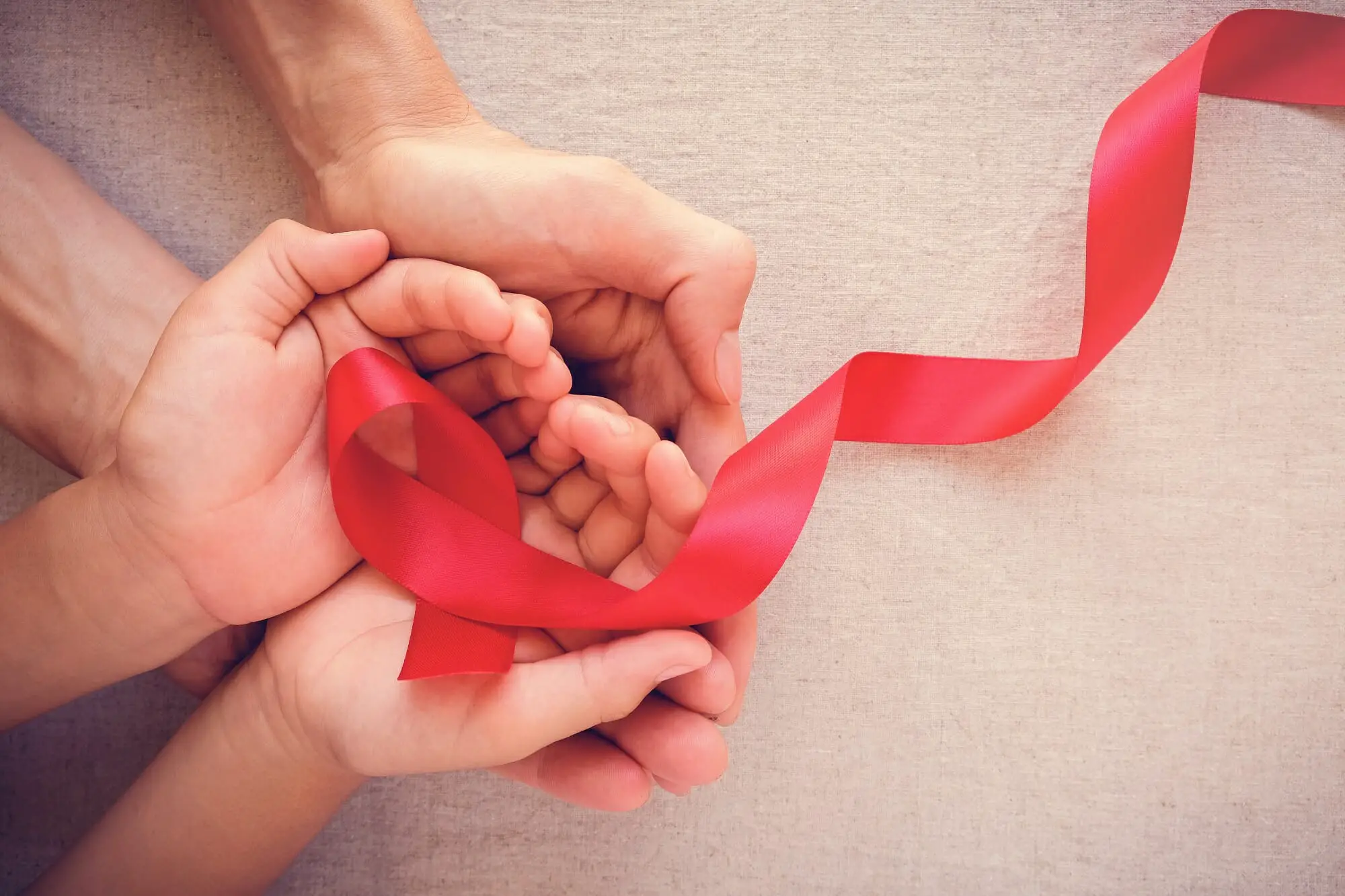 adult and child hands holding red ribbon, hiv awareness concept